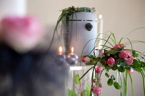 Blumenschmuck mit rosa Rosen und grünen Pflanzenarrangements auf einem Tisch, umgeben von Kerzen und einem weißen Behälter.