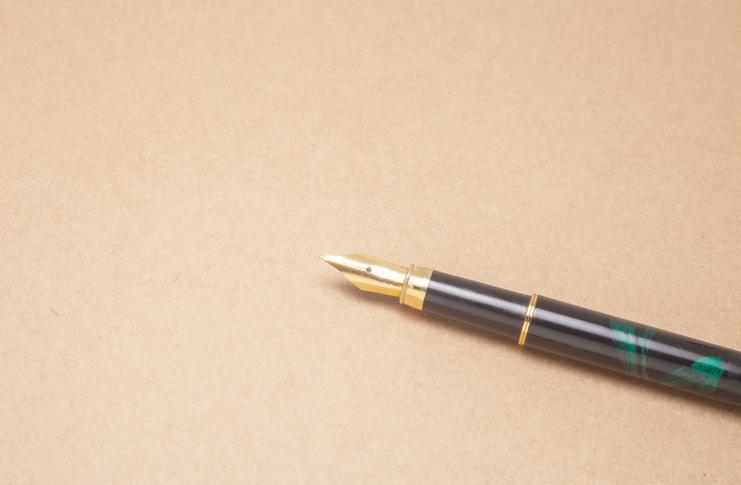 Nahaufnahme einer Füllfeder mit goldener Spitze auf einer braunen, strukturierten Unterlage.